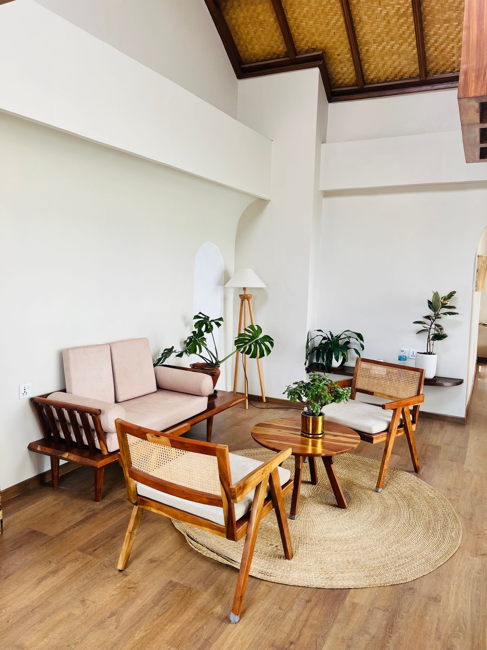 Boho sitting area with cane-backed rattan chairs, a floor lamp, layered plants and a woven round rug