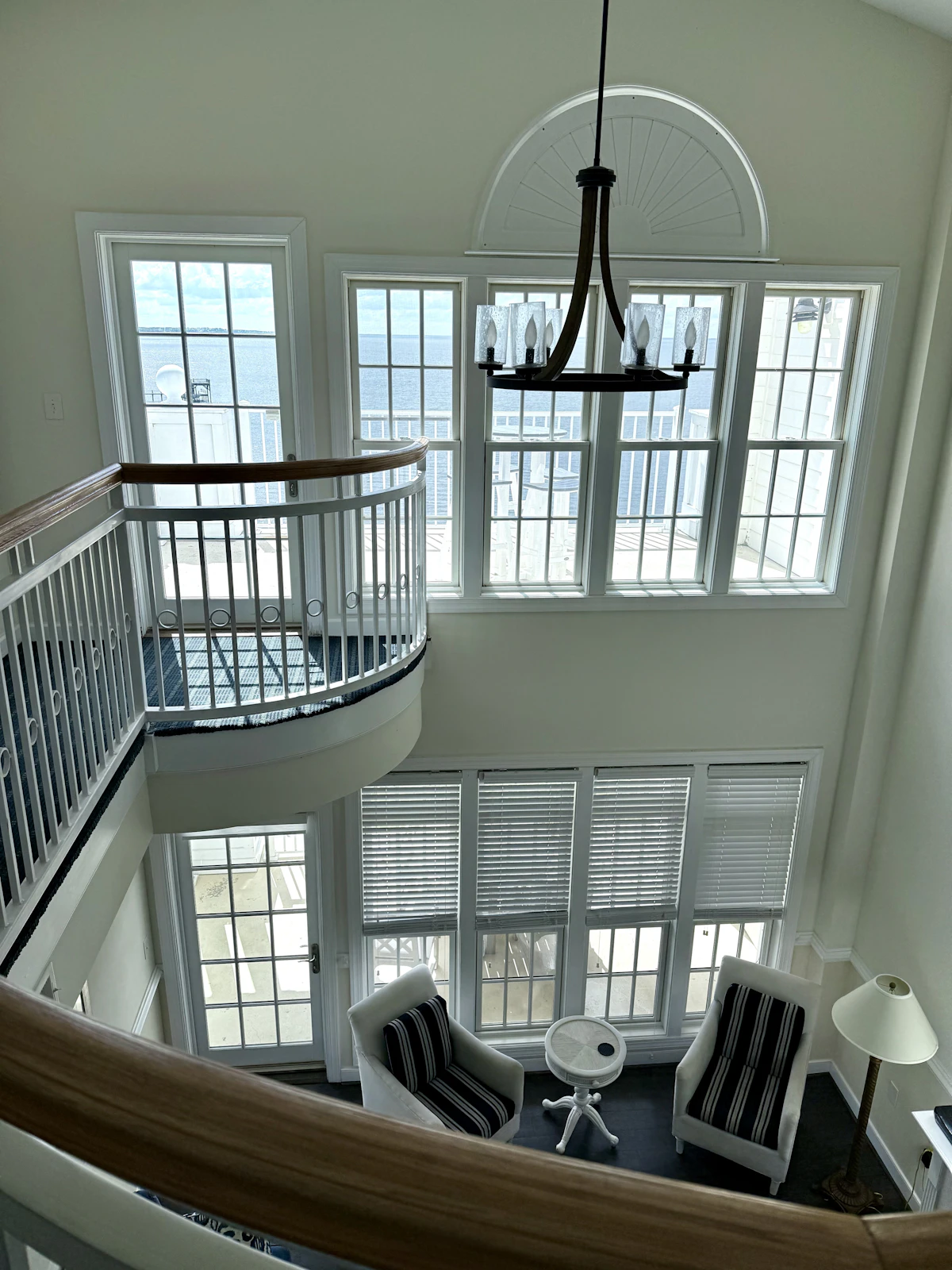 Bright coastal-style great room with white trim, tall windows overlooking the water and striped navy-and-white armchairs