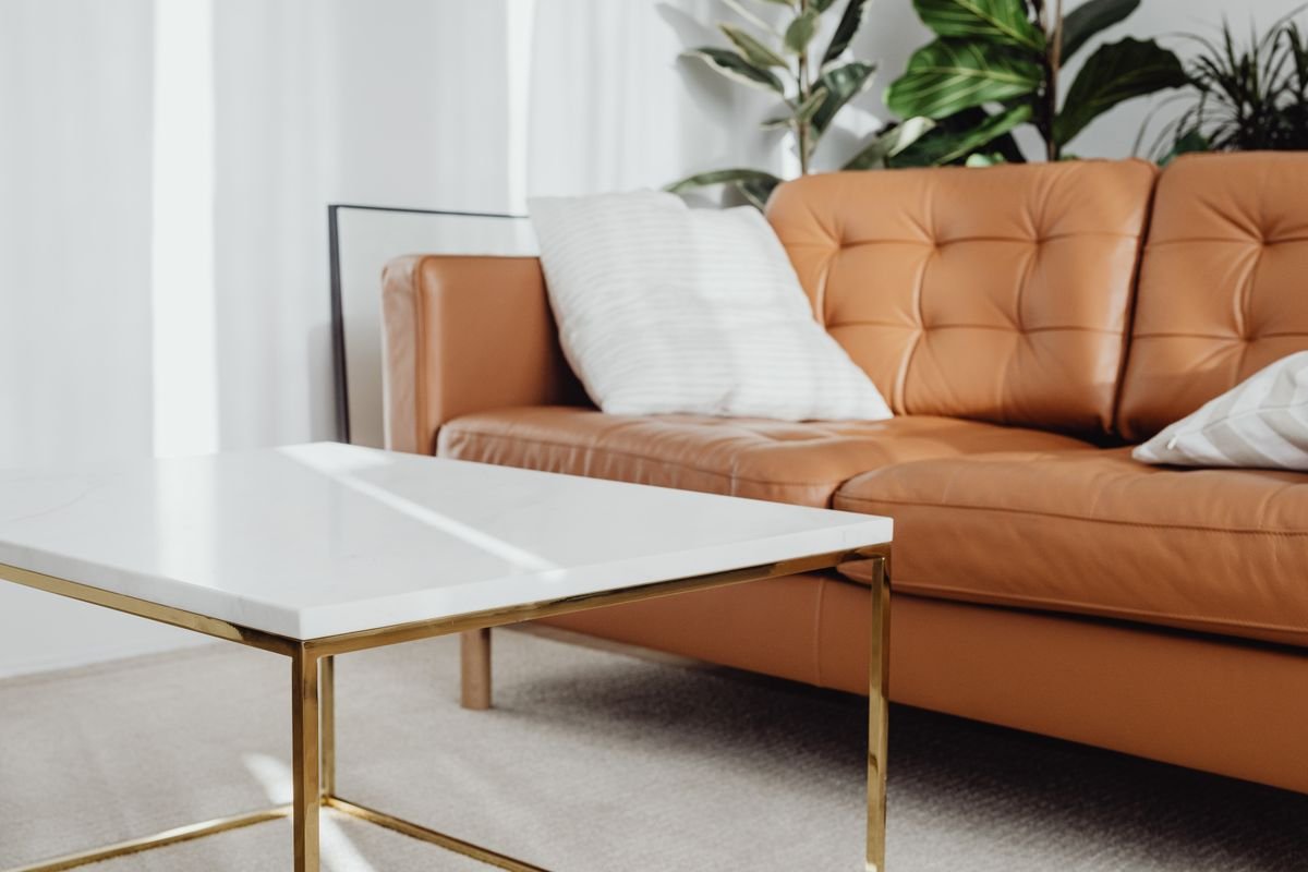 Contemporary living room corner with a tufted cognac leather sofa, a brass-framed marble coffee table and layered plants