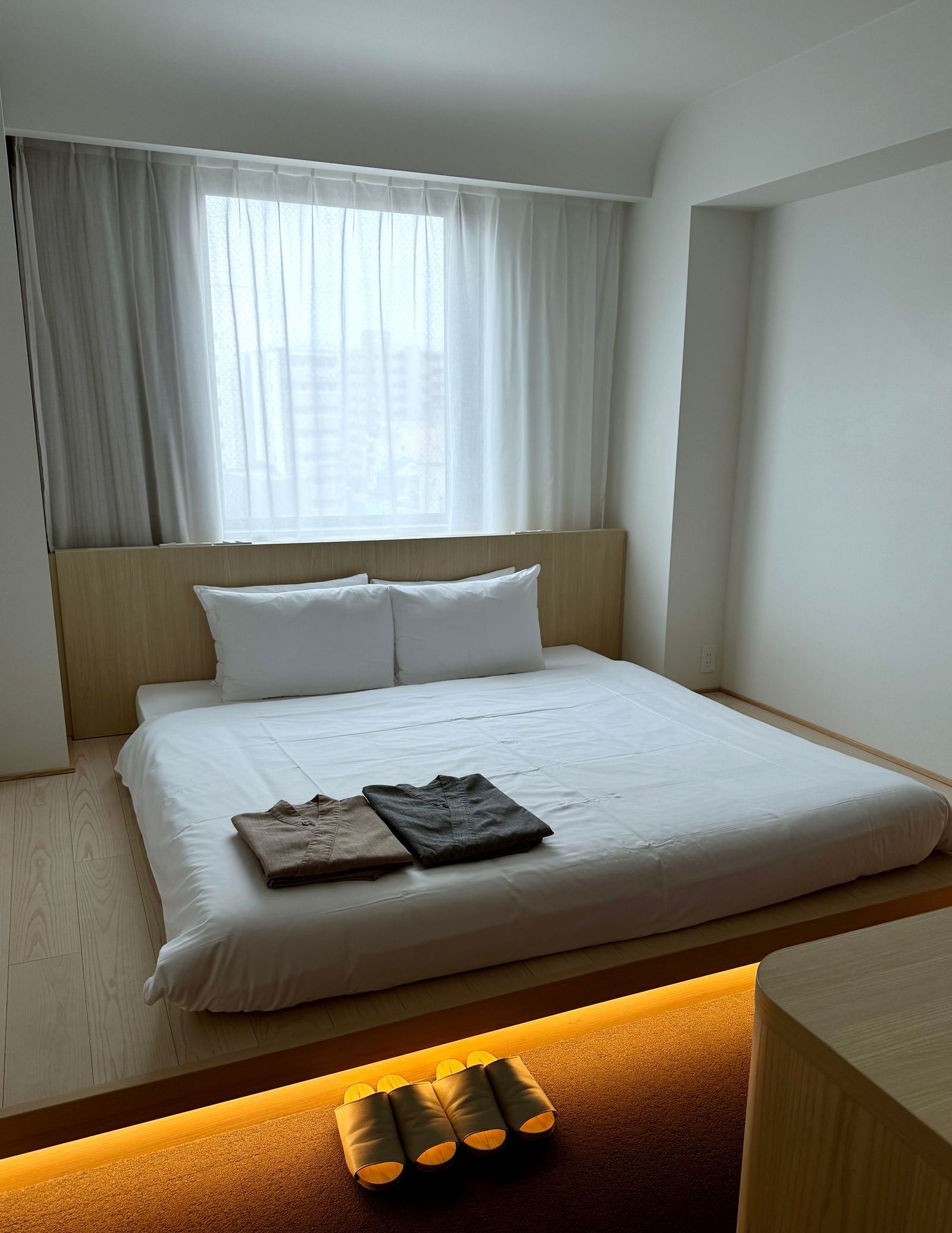 Japandi-style bedroom with a low wood platform bed, white bedding and a sheer curtained window