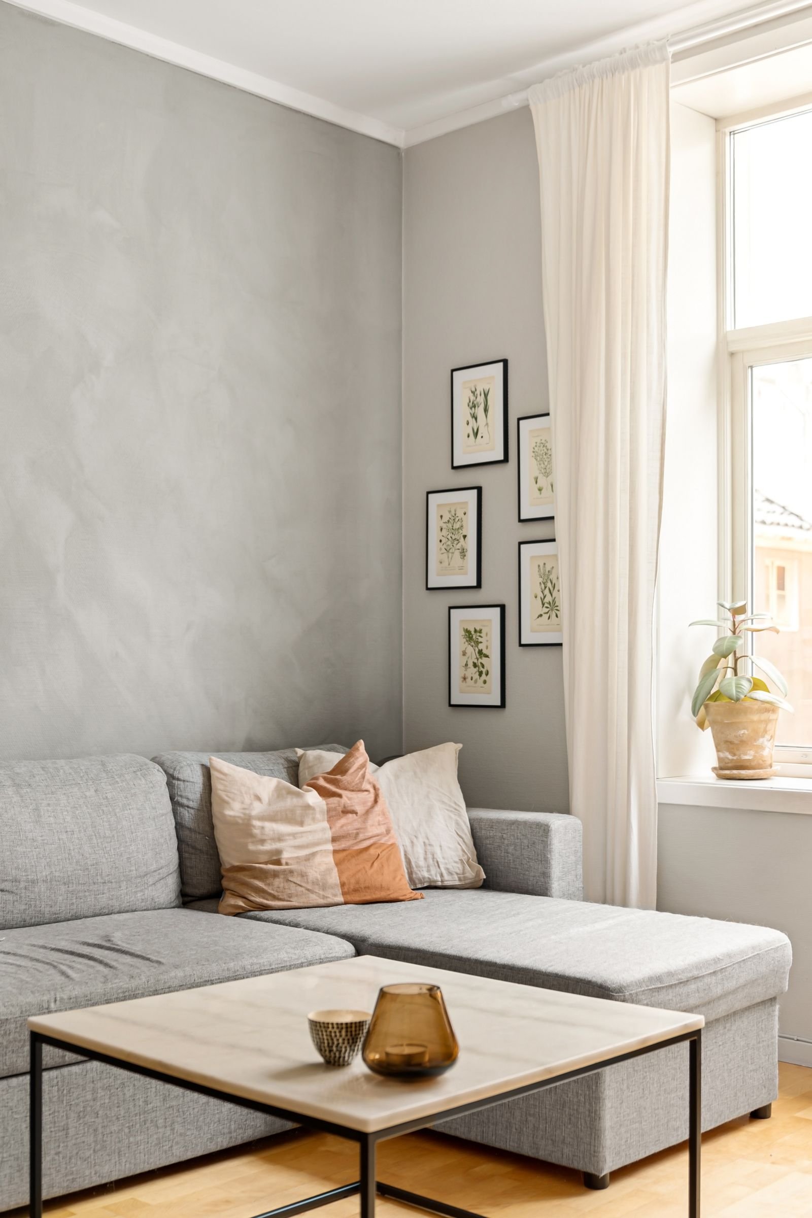 Minimalist living room with a grey sectional sofa, botanical gallery wall and a marble coffee table