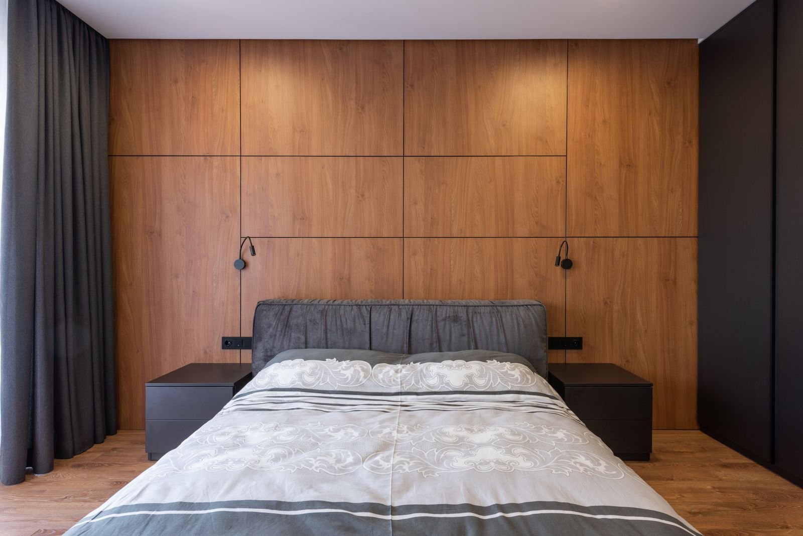 Modern bedroom with a walnut-paneled wall, upholstered gray headboard and dark matching nightstands