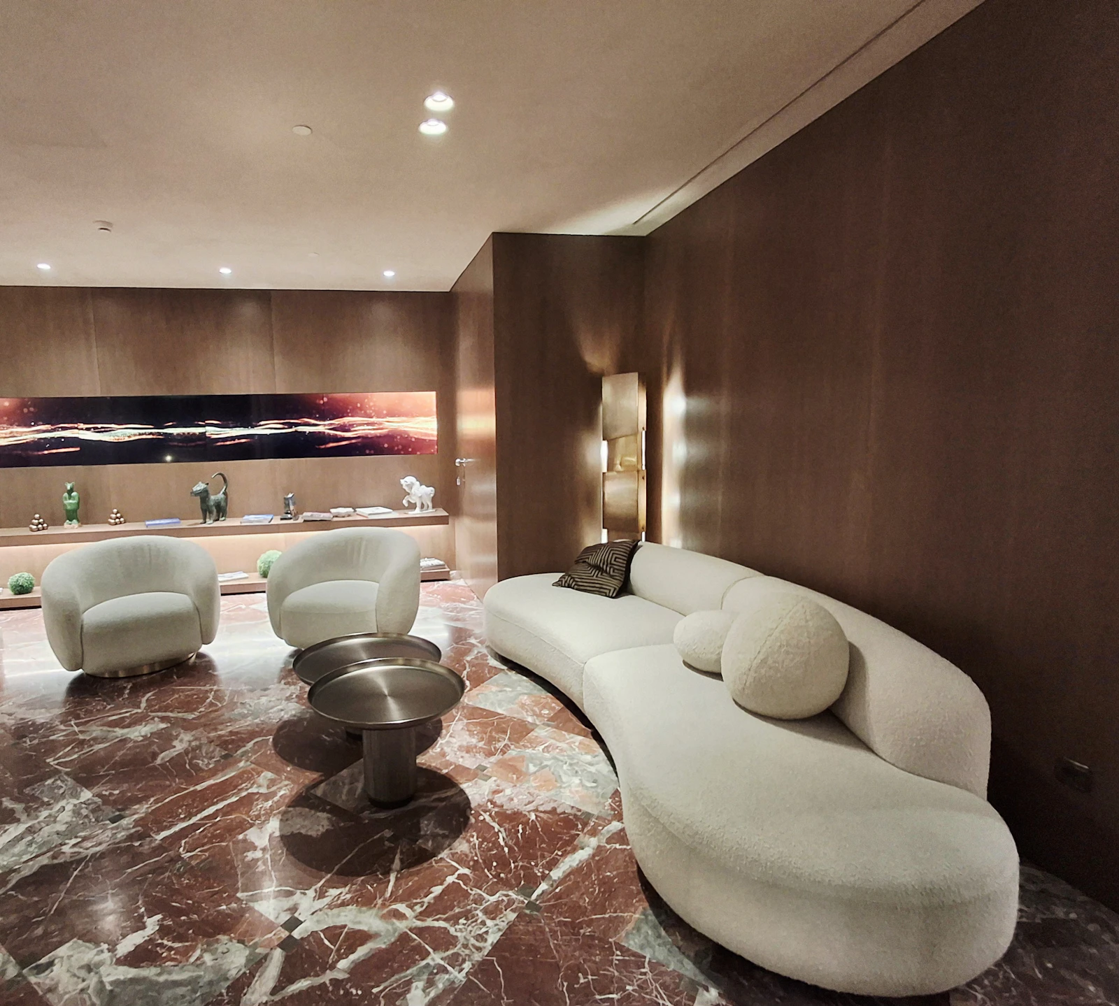 Elegant living room with a curved bouclé sofa, marble floor and warm layered wall lighting