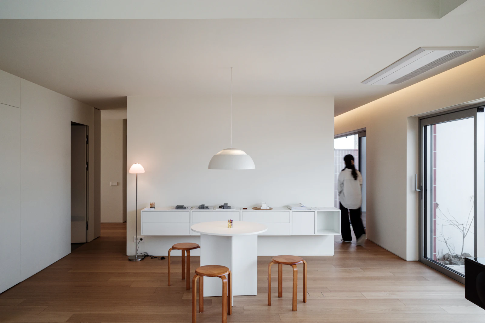 Minimalist dining nook with a round white table, bentwood stools and a dome pendant light