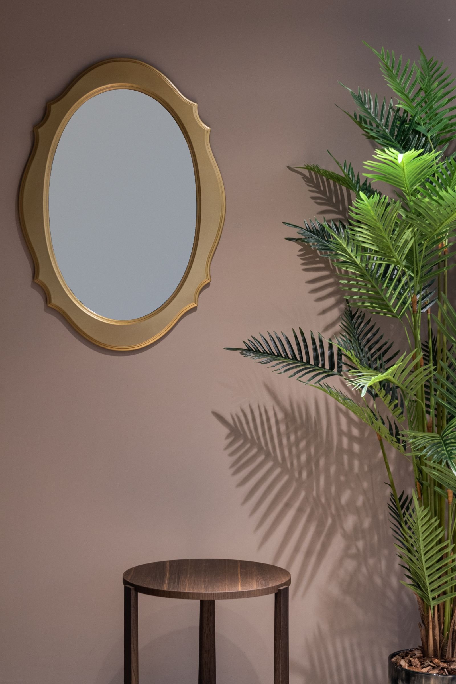 Simple styled corner with a gold oval mirror, a wood side table and a tall potted palm