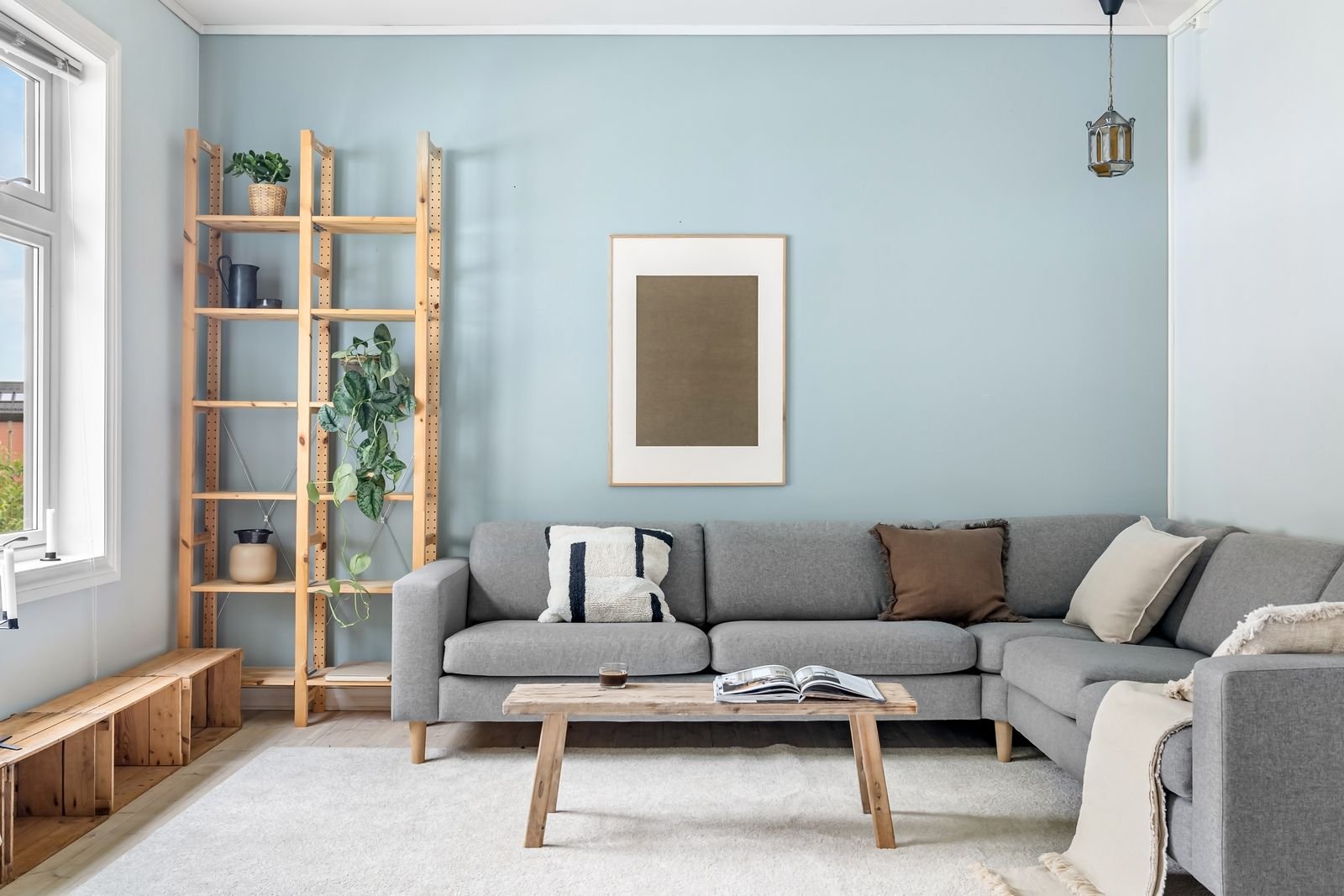 Bright Scandinavian living room with a light wood ladder shelf, grey sofa, wood coffee table and cream rug