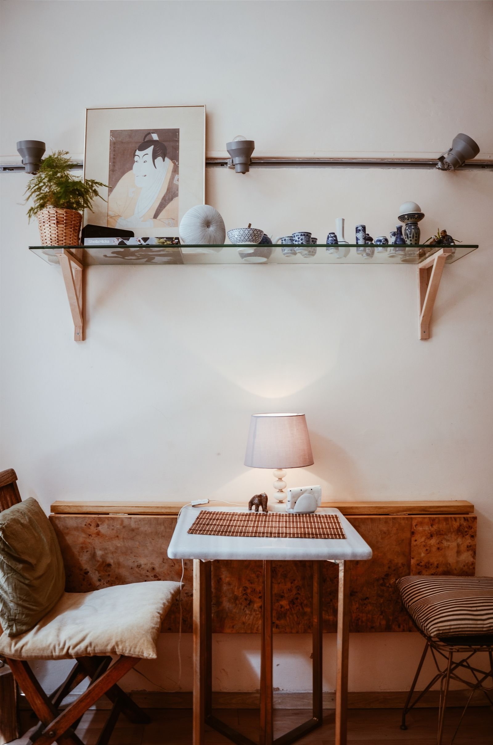 Simple styled console table with a lamp, framed art and a glass shelf of small decorative objects