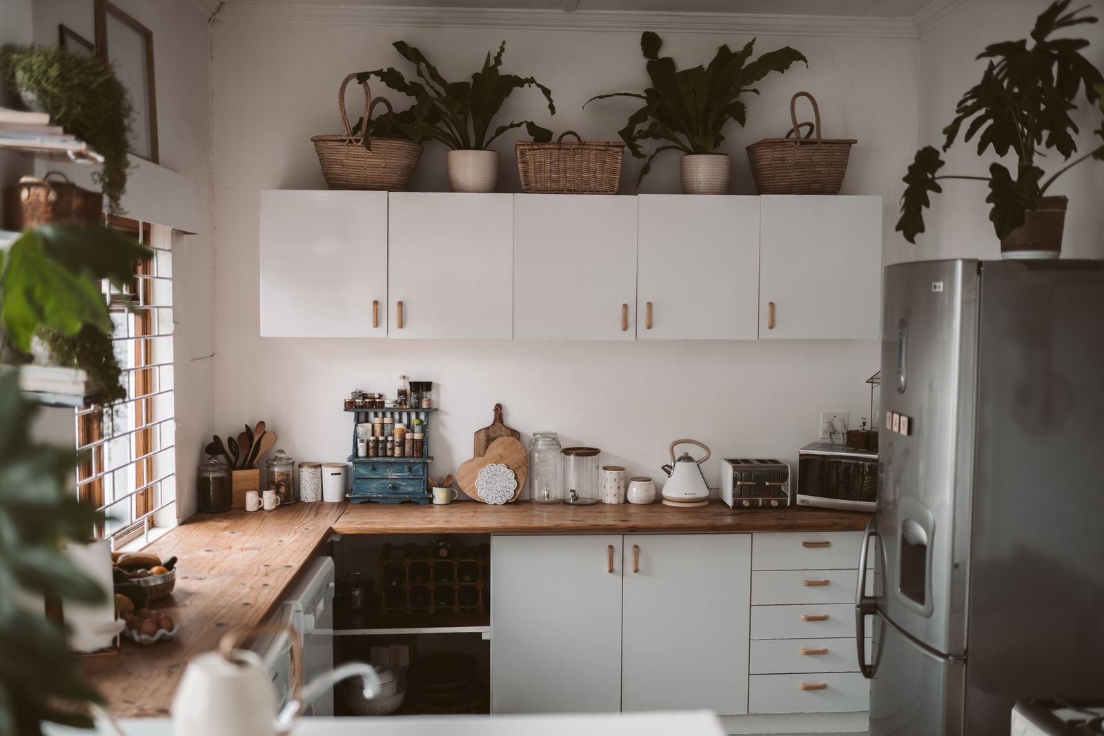 Bright kitchen with painted cabinets, wicker baskets and trailing plants styled on top, and ceramic jars on the counter